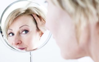 A mature woman in her 60's looking in a makeup mirror for her daily beauty routine.