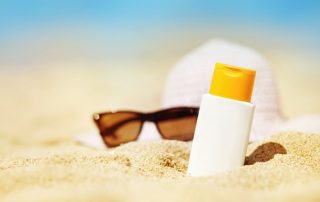 A picture of sunscreen and sunglasses lying in the sand on the beach