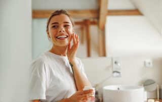 A woman applying a facial cream while smiling.