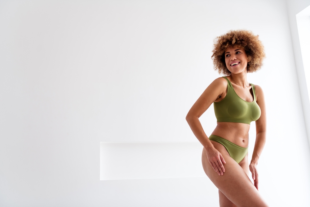 A woman smiling while posing in a green matching underwear set.