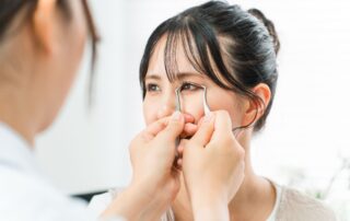 Provider using a curved instrument to assess a woman's upper eyelid during a blepharoplasty consultation